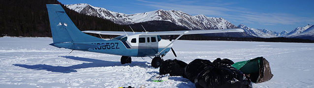 A blue and white airplane parked in snow with trash bags in foreground. A blue and white airplane parked in snow with trash bags in foreground.