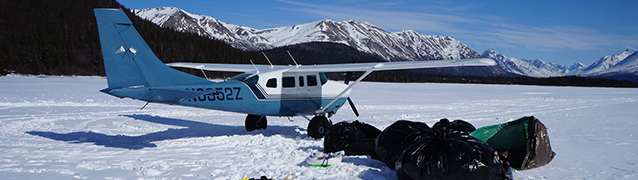 A blue and white airplane parked in snow with trash bags in foreground.