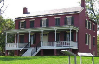 A two-story red farmhouse has a porch across its front length and two chimneys. A two-story red farmhouse has a porch across its front length and two chimneys.