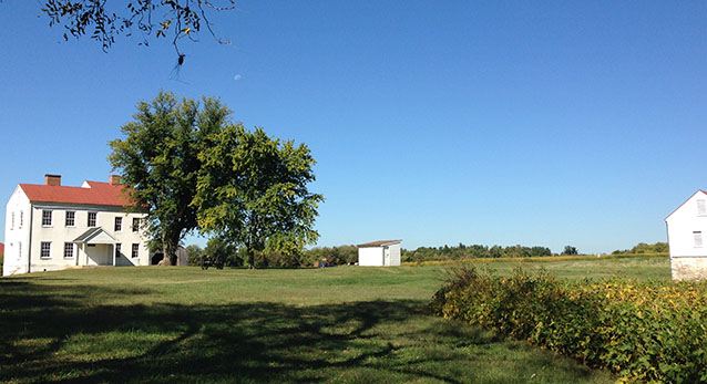 A two-story farm house beside a tree, in an open agricultural landscape with fields and outbuildings A two-story farm house beside a tree, in an open agricultural landscape with fields and outbuildings