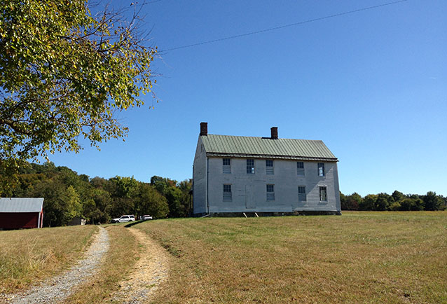 Dirt tire tracks curve toward a two-story farmhouse under clear sky. Dirt tire tracks curve toward a two-story farmhouse under clear sky.