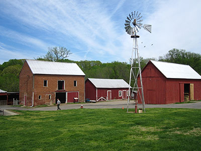 A row of farm buildings and a windmill beyond a swatch of green grass.