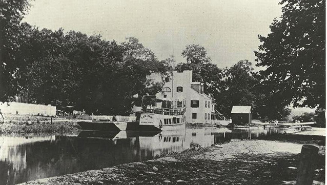 Canal boat "Louise" in still canal water beside the two story Great Falls Tavern