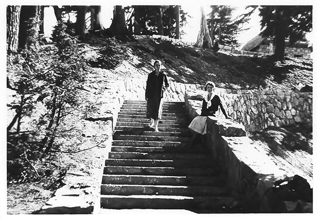 Two women on a wide stone stairway, one seated on the stone wall and one standing. 