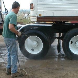  A man sprays the tires of a vehicle with a hose.