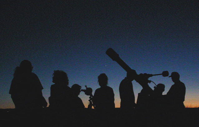 silhouettes of 7 people and telescopes in front of a night sky. 