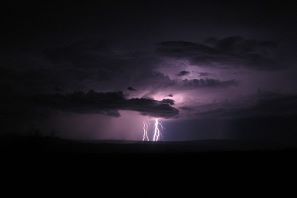 Dramatic lightning at night casting a purple light in the clouds.