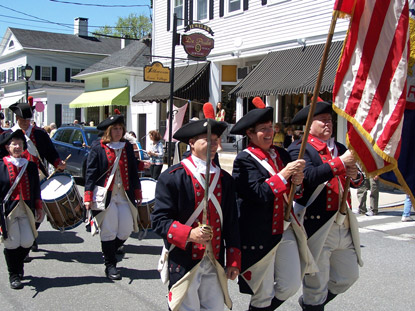 War of 1812 reinactors march down a main street holding flag War of 1812 reinactors march down a main street holding flag