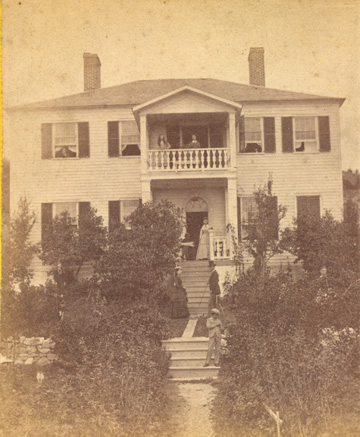 Photograph of a house with an American Indian entrepreneur standing on porch