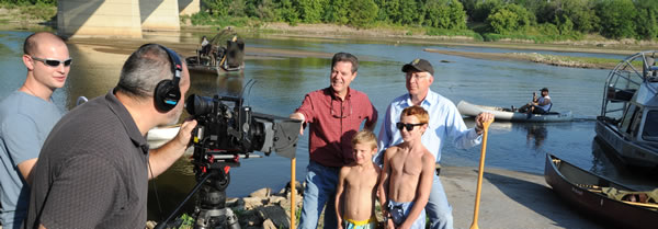 Camerman filming four people posing in front of the river.