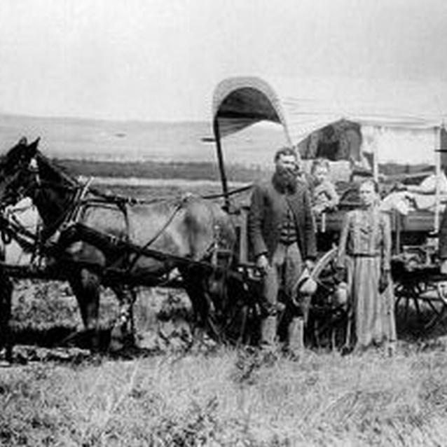 Photo of a young family with their covered wagon and team of horses.
