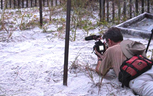 A member of the film crew records footage on the beach