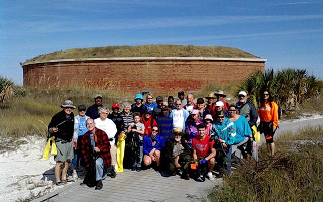 Volunteers and a ranger on the boardwalk near a brick fort called Massachusetts.