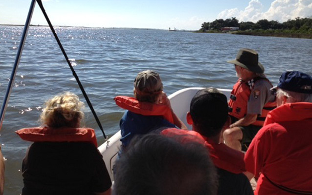 A park ranger interprets bayou dynamics to visitors in a boat on the water.