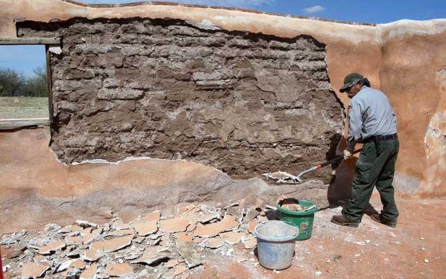 park maintenance worker shoveling broken plaster with exposed adobe underneath