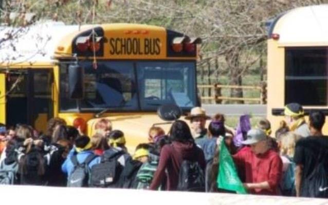 Kids gather around a park ranger near school busses.