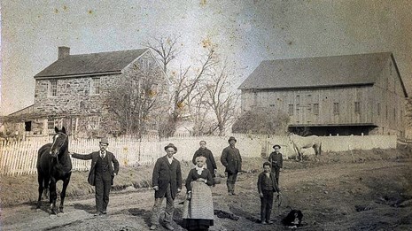 A black and white photograph of a black family posing with a white man and his horse in a dirt road.