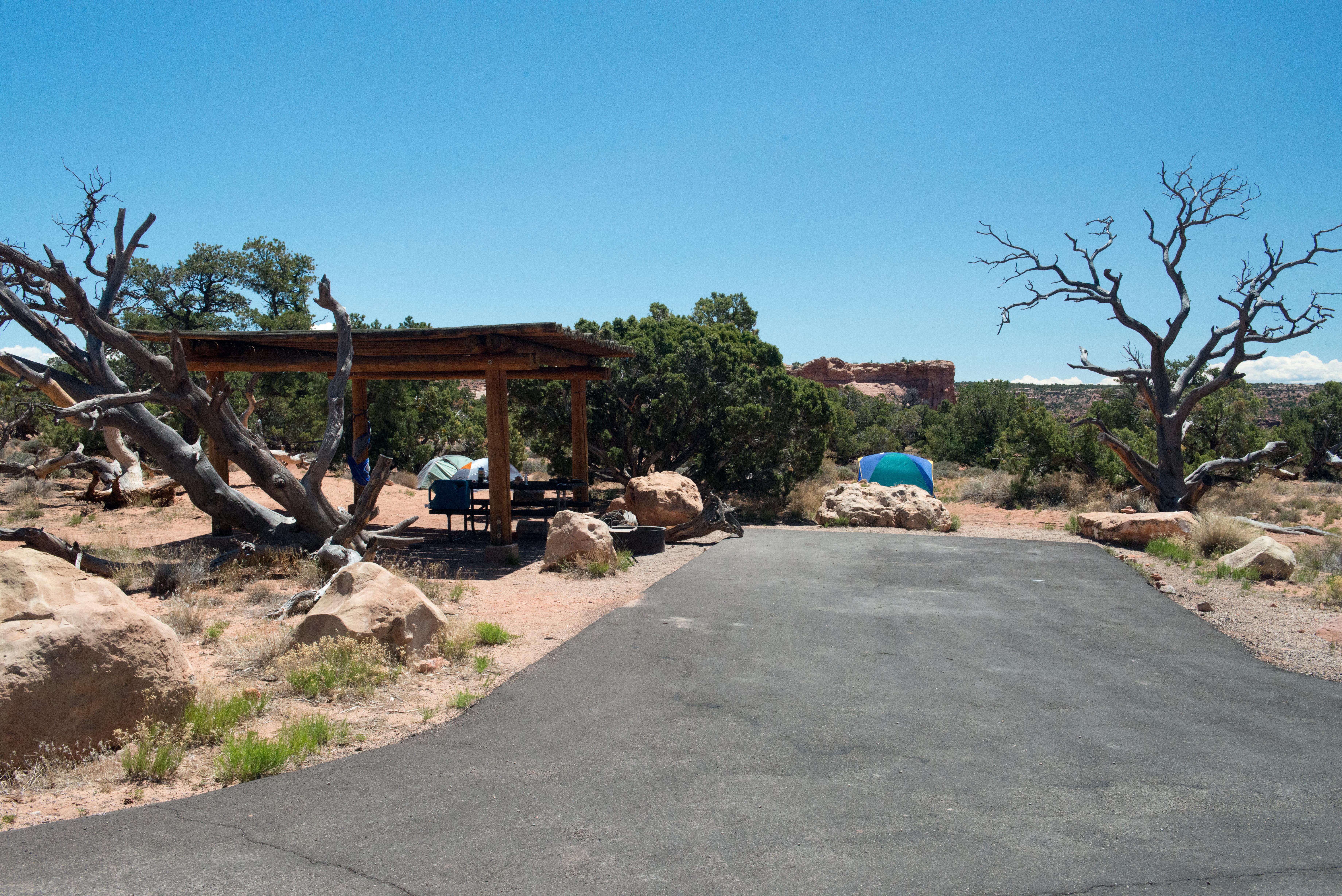 a paved driveway with a shade structure and two tents in the background