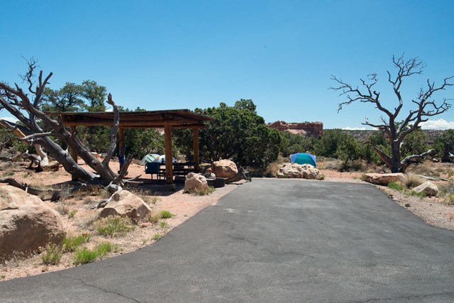 A paved driveway with a shade structure and two tents in the background at a campsite
