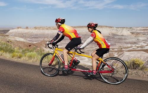 Two people in colorful clothing on a tandem bicycle with banded badlands in the background
