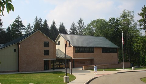 Two-story brick visitor center with a green metal roof, lawn and a flagpole