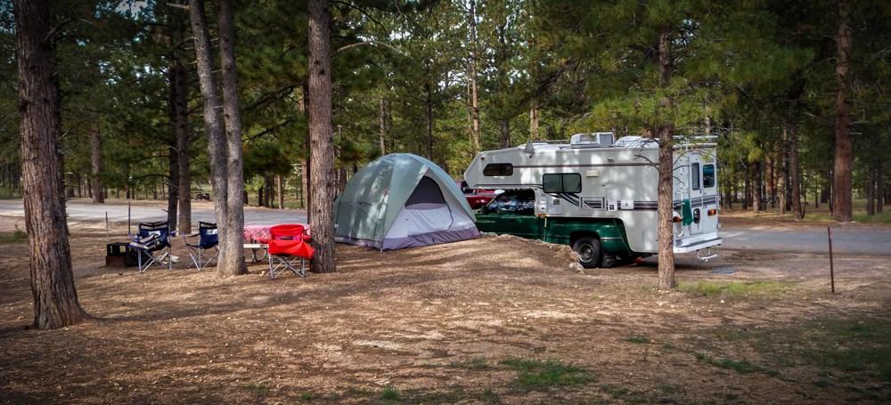 Camping chairs, a tent, and camper at a campsite.