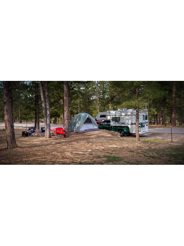 Camping chairs, a tent, and camper at a campsite.