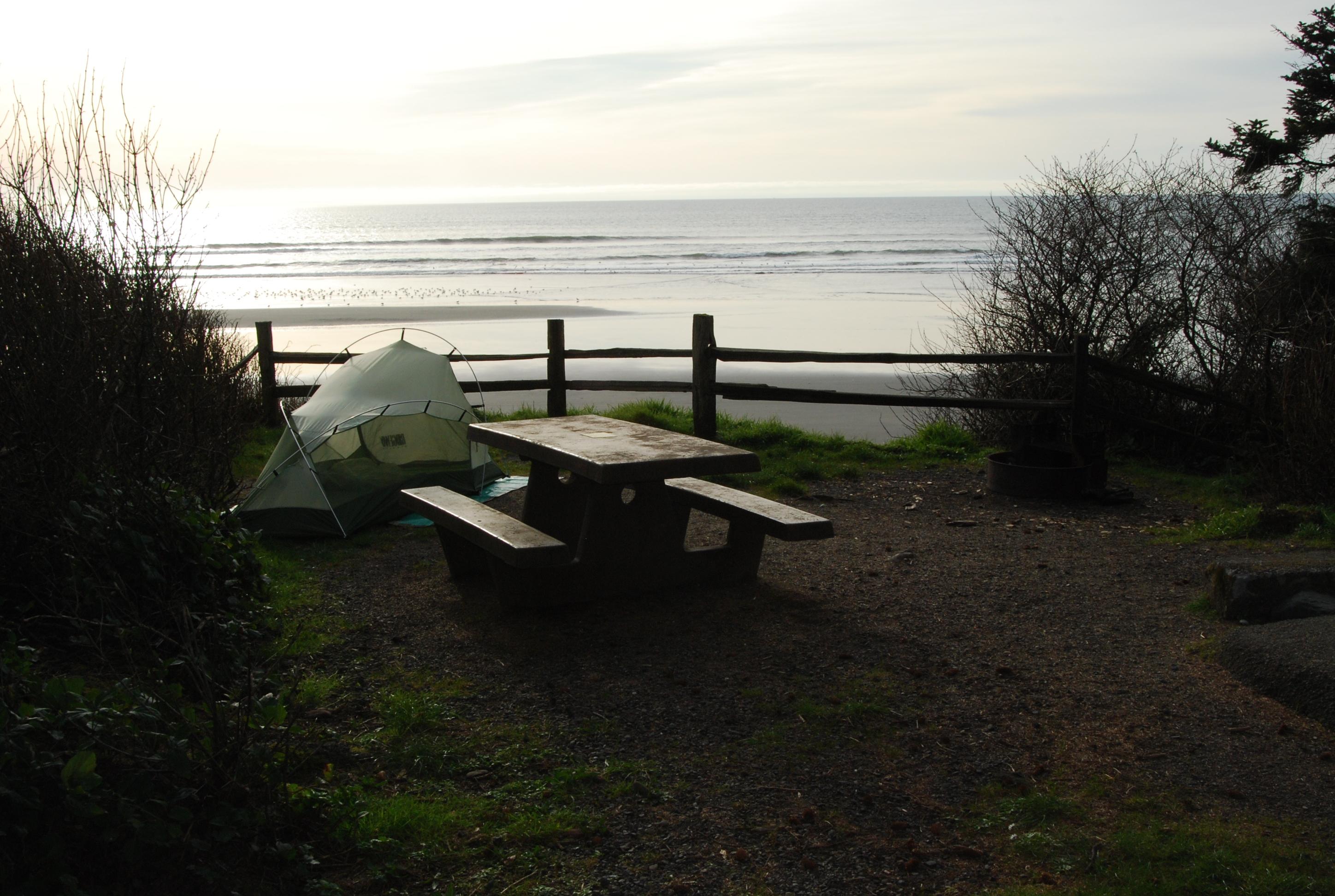 A campsite with a picnic table and tent, overlooking the ocean.