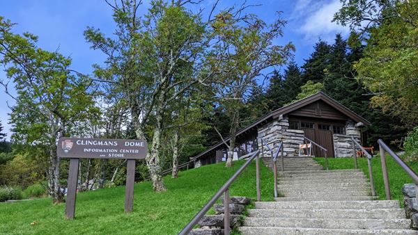 A sign that says "Clingmans Dome Information Center & Store" beside stairs near a brick building