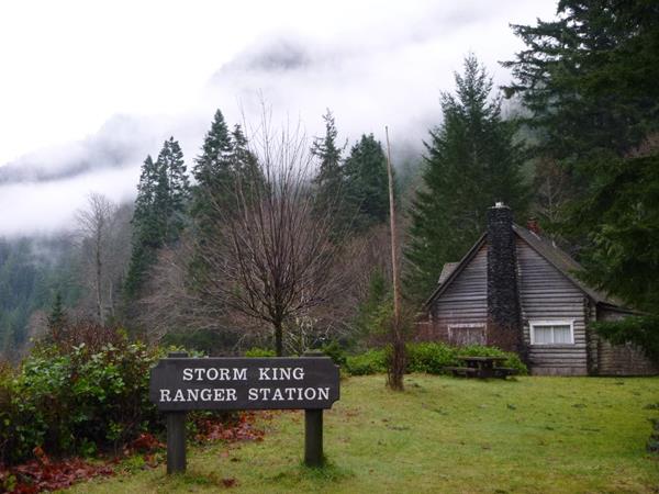 A log cabin with a chimney. A sign outside reads "Storm King Ranger Station."