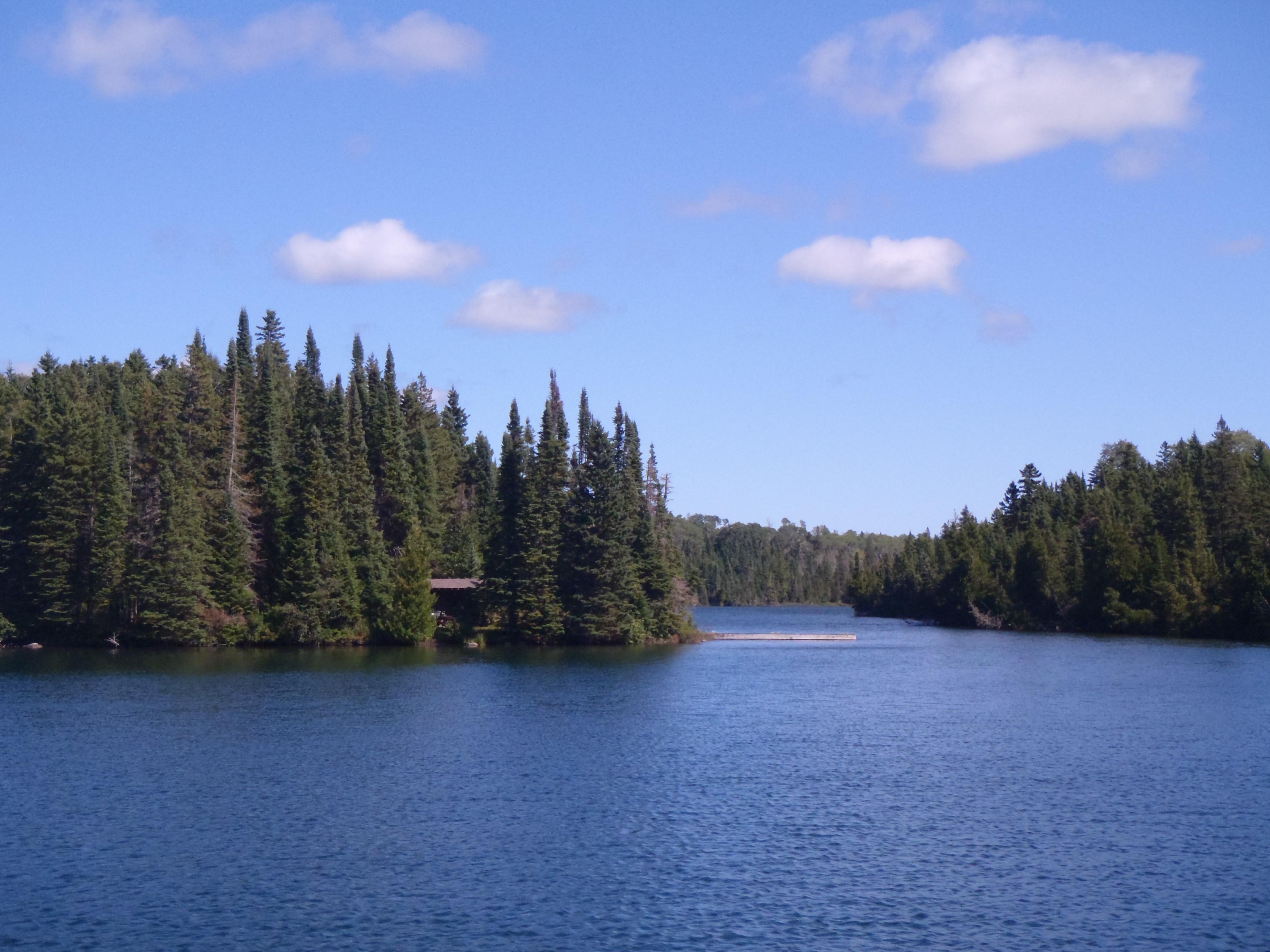 Birch Island Campground shelter visible across water through tress with a blue sky overhead.