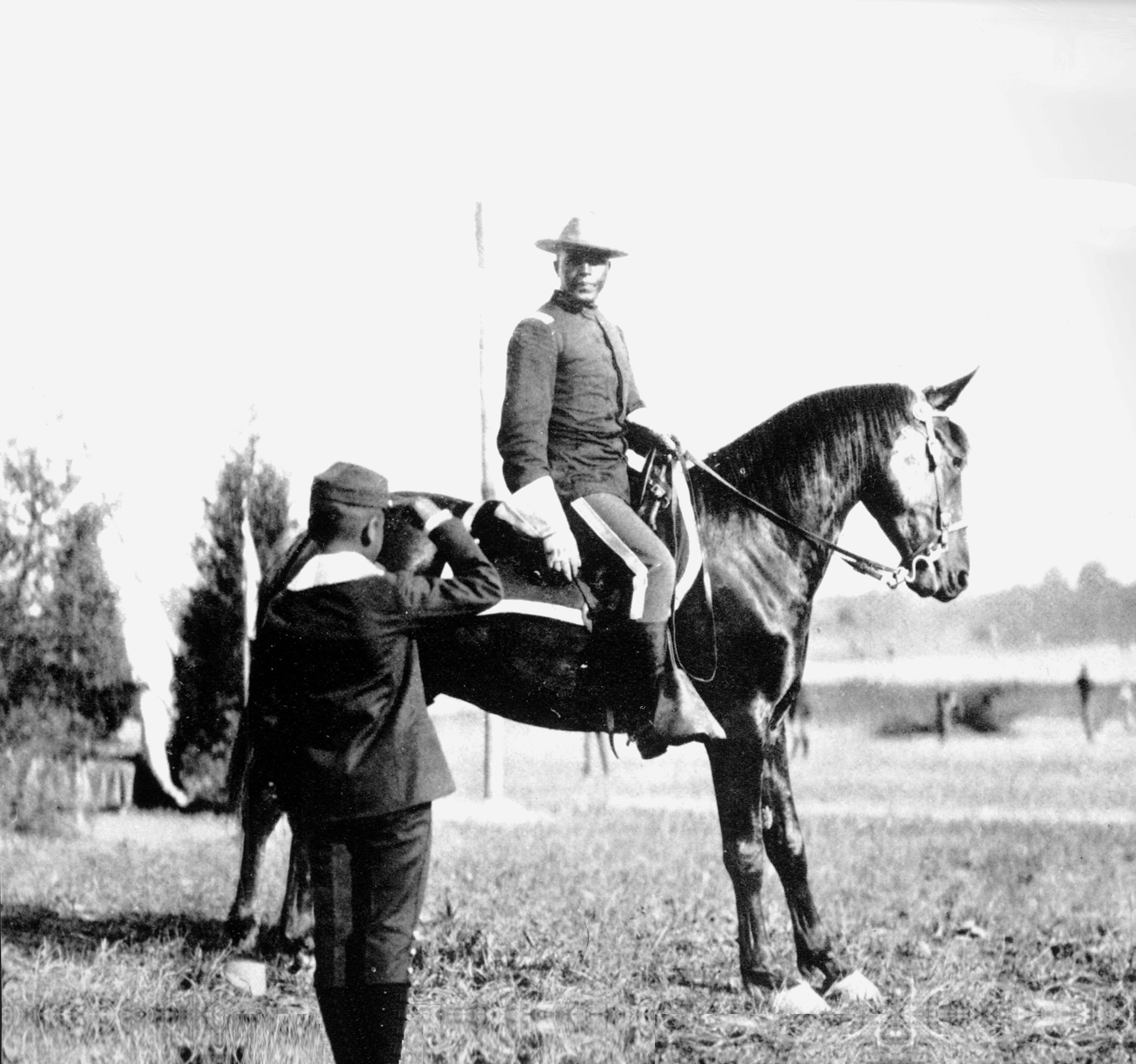 An African American man in a military uniform sitting high on a horse being saluted by a boy