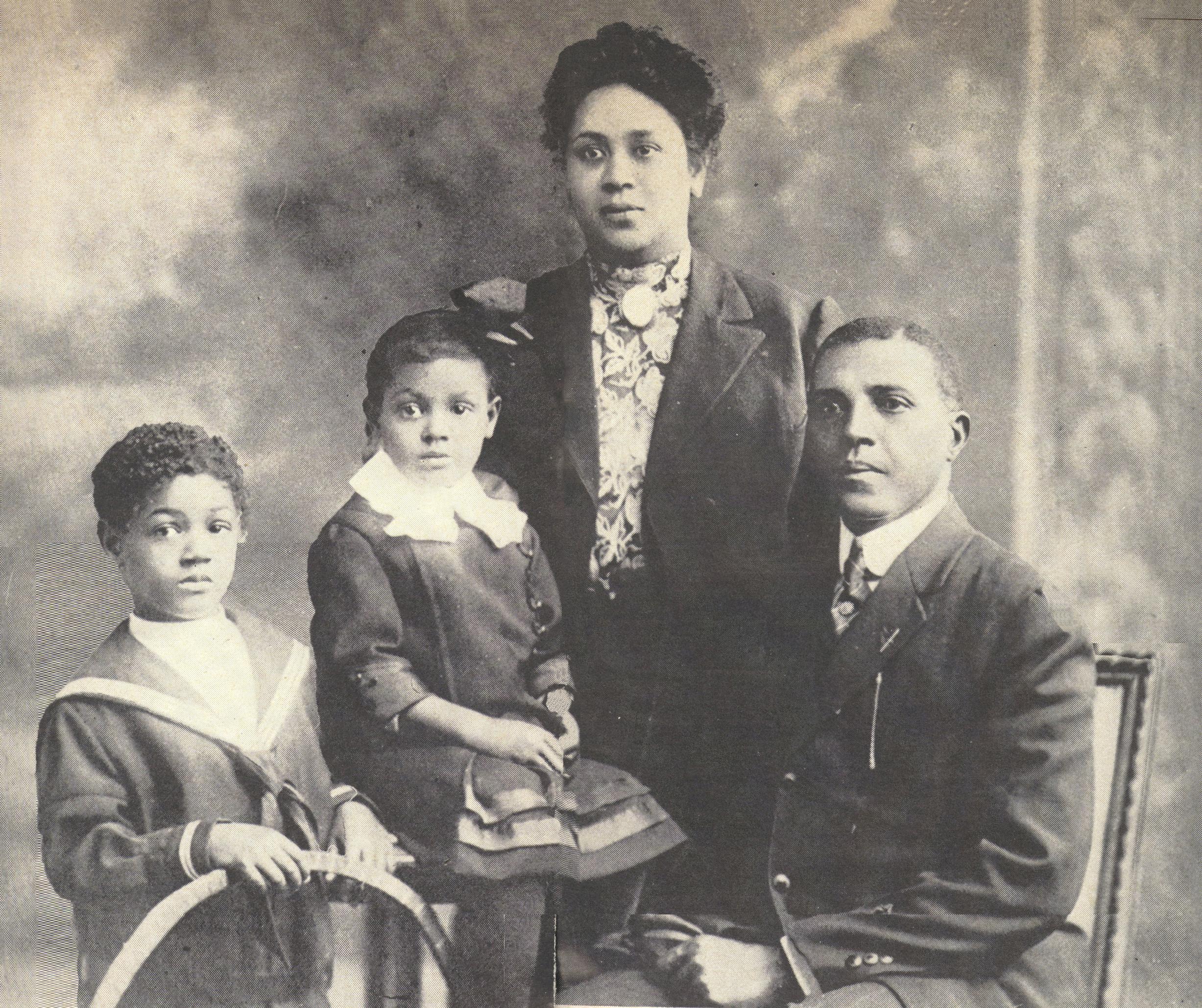 An african american family posing for a portrait with the mother standing behind the father and kids