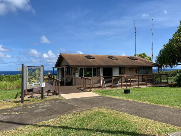 A small brown building stands out in front of a bright blue sky and ocean.