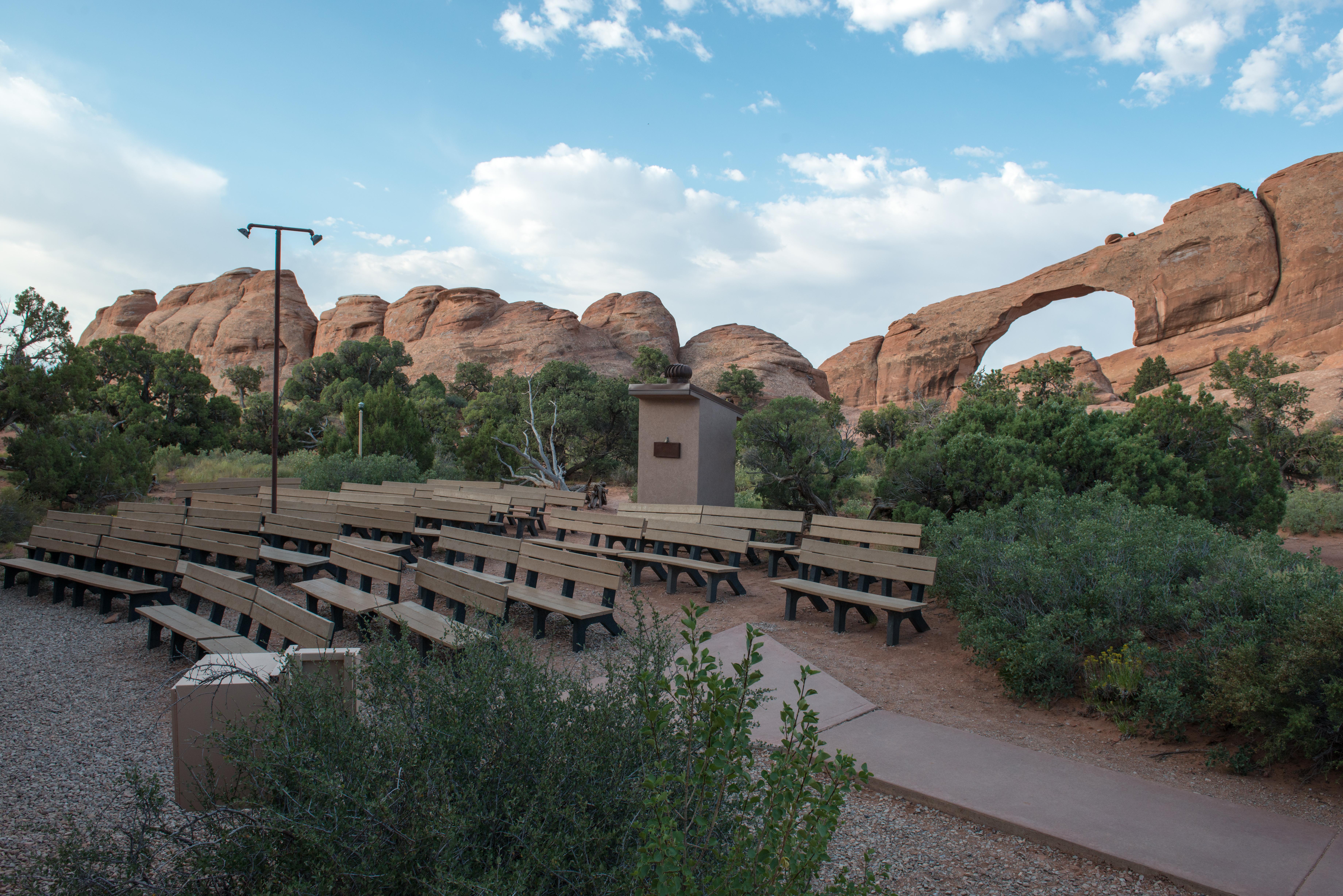 several benches sit in a semi circle with a broad, stone arch in the background