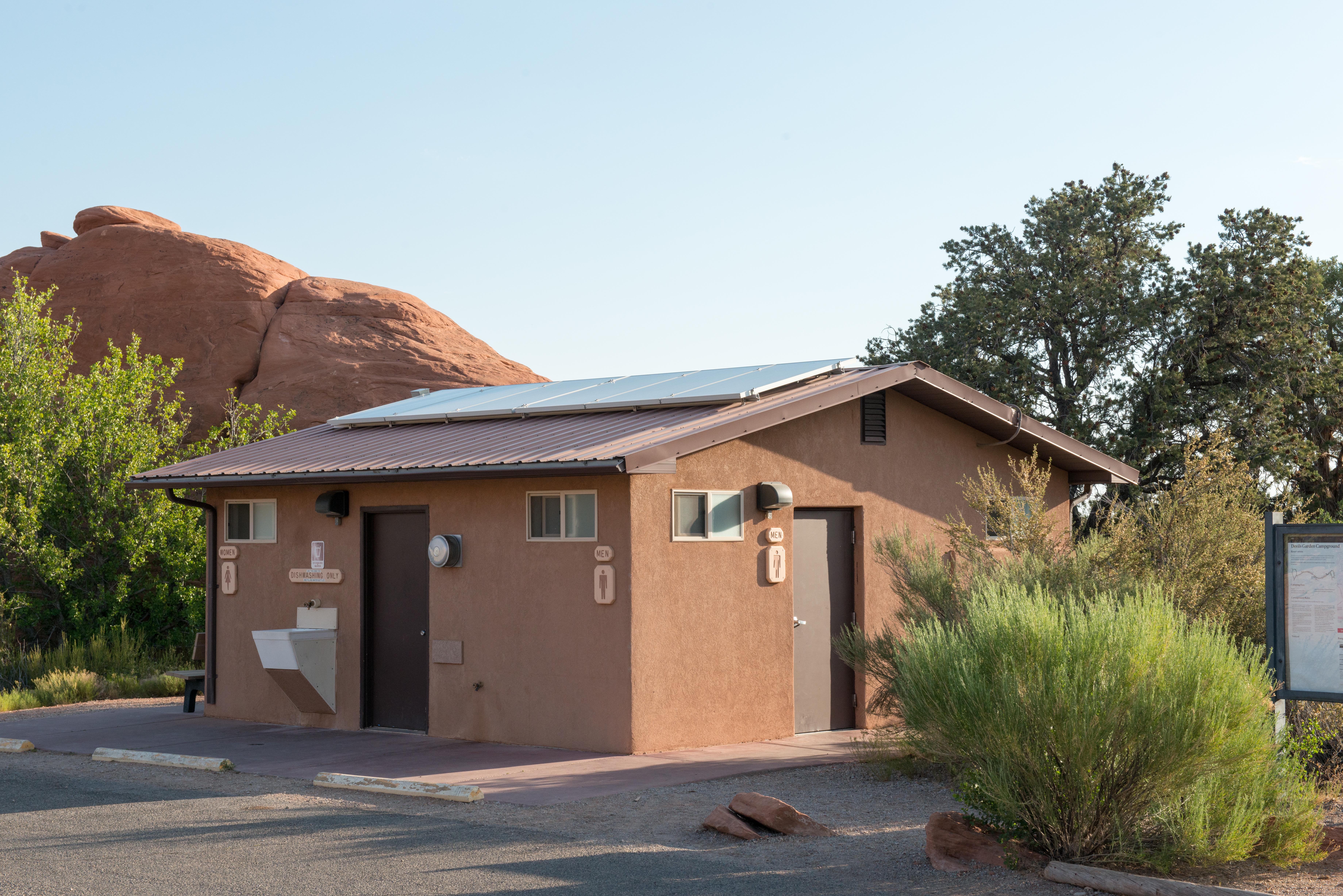 A small, brown building with men's and women's restroom signs and an outdoor sink