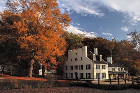 White 18th-century-style tavern building among bright orange autumn trees beside the canal
