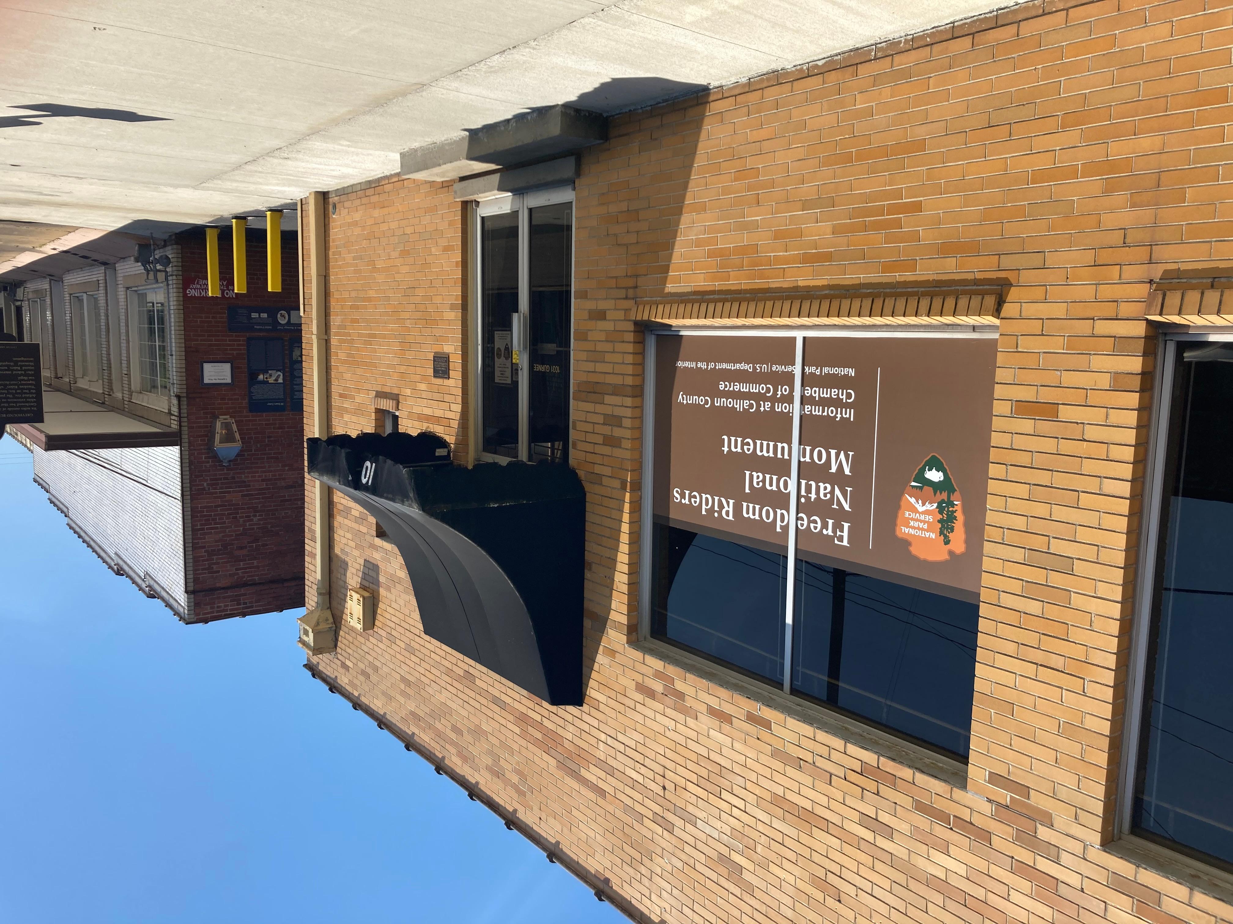 street view of a yellow brick bus depot, with a black awning and NPS sign, and an alley entrance.