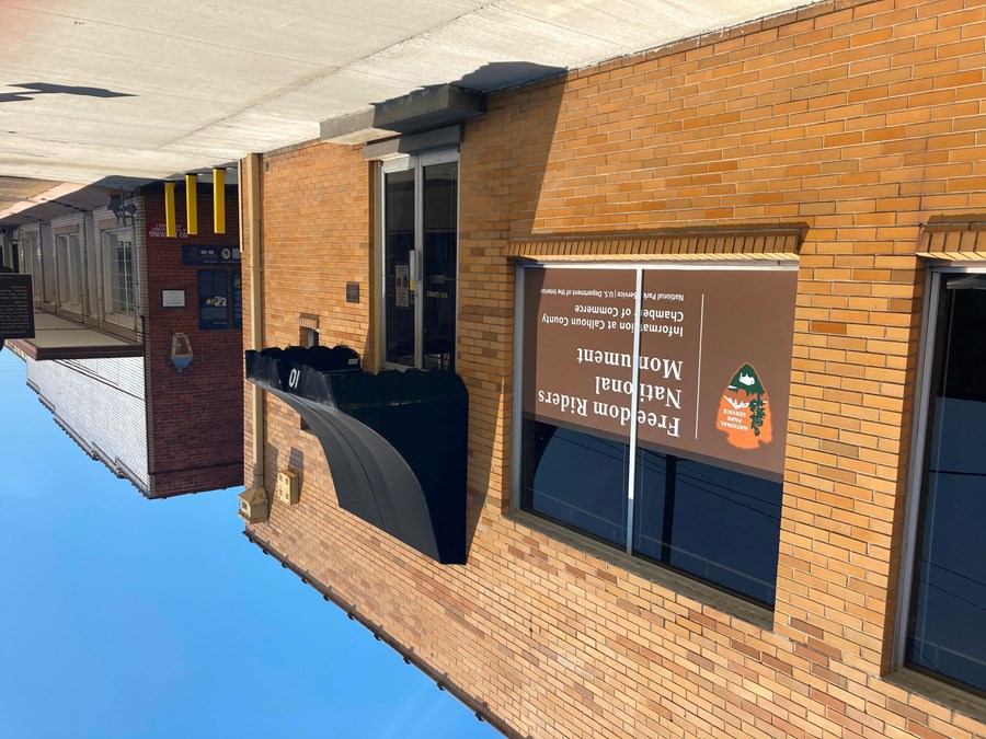 street view of a yellow brick bus depot, with a black awning and NPS sign, and an alley entrance.