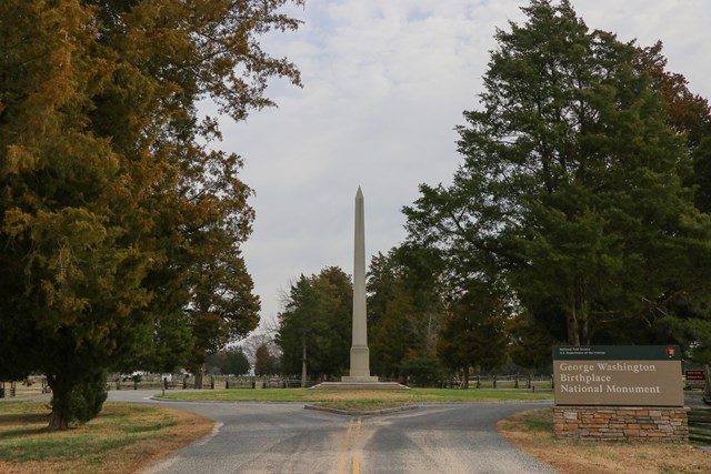 White obelisk in a roundabout, surrounded by trees and the park sign