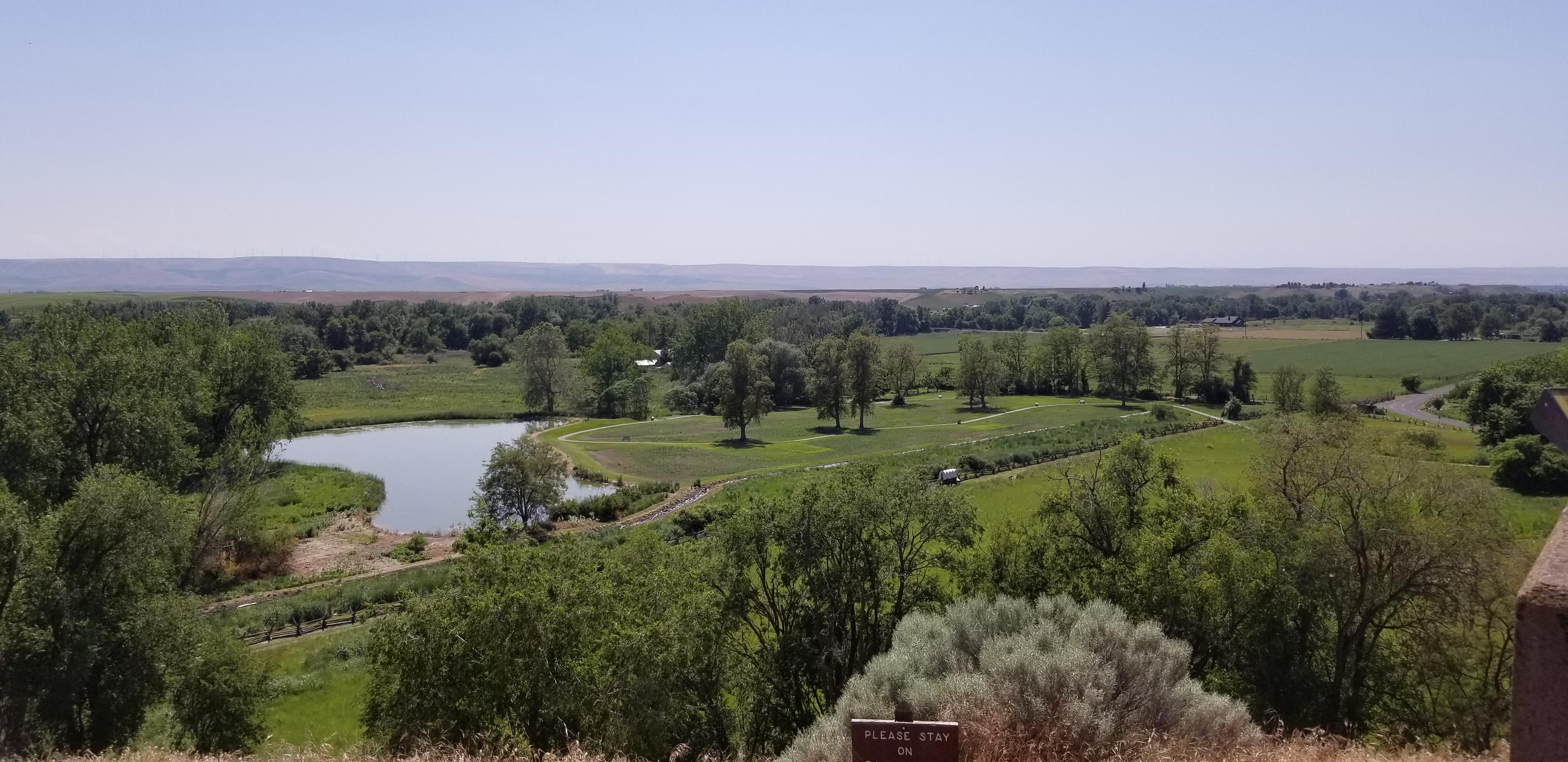 View from above looking down at green fields, a pond, and mountains in the distance