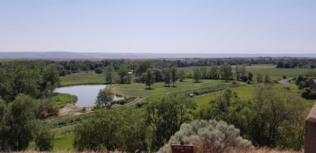 View from above looking down at green fields, a pond, and mountains in the distance