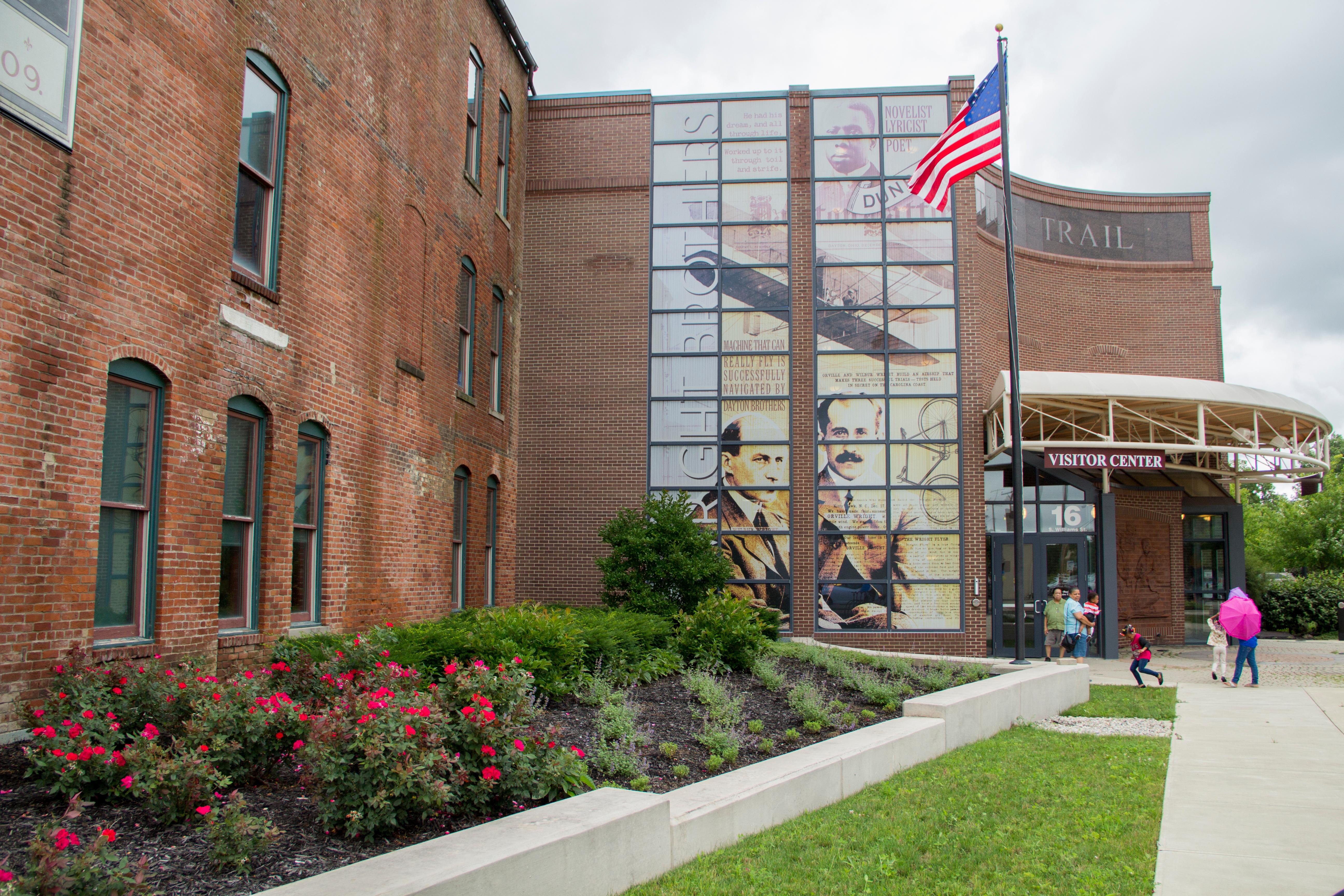 A three-story brick building with tall green windows and a tall photo mural on the glass wall