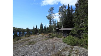 Rocky shoreline with two shelters along the treeline with blue sky overhead.