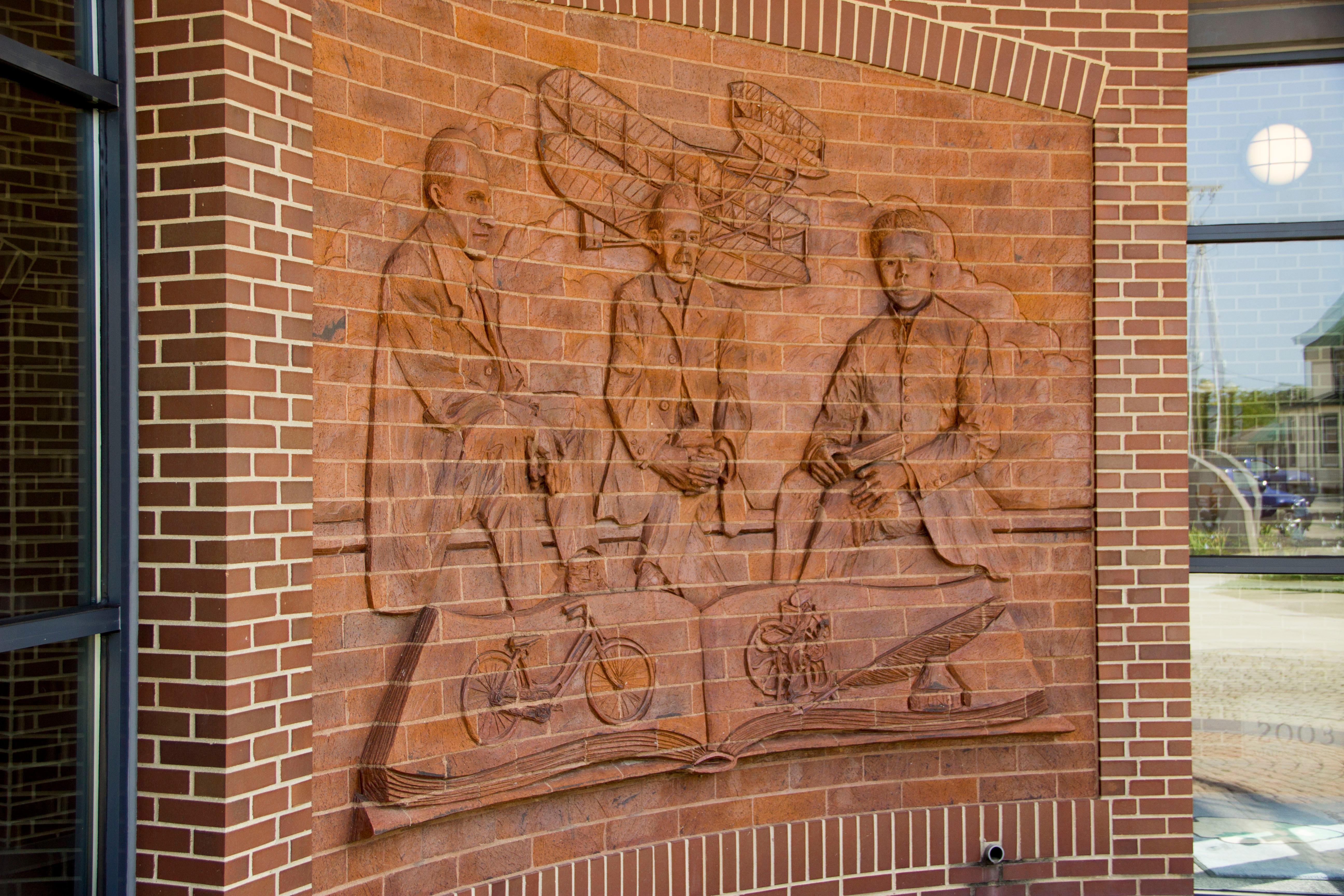 A brick wall with artwork of three men and an airplane etched out of the brick.