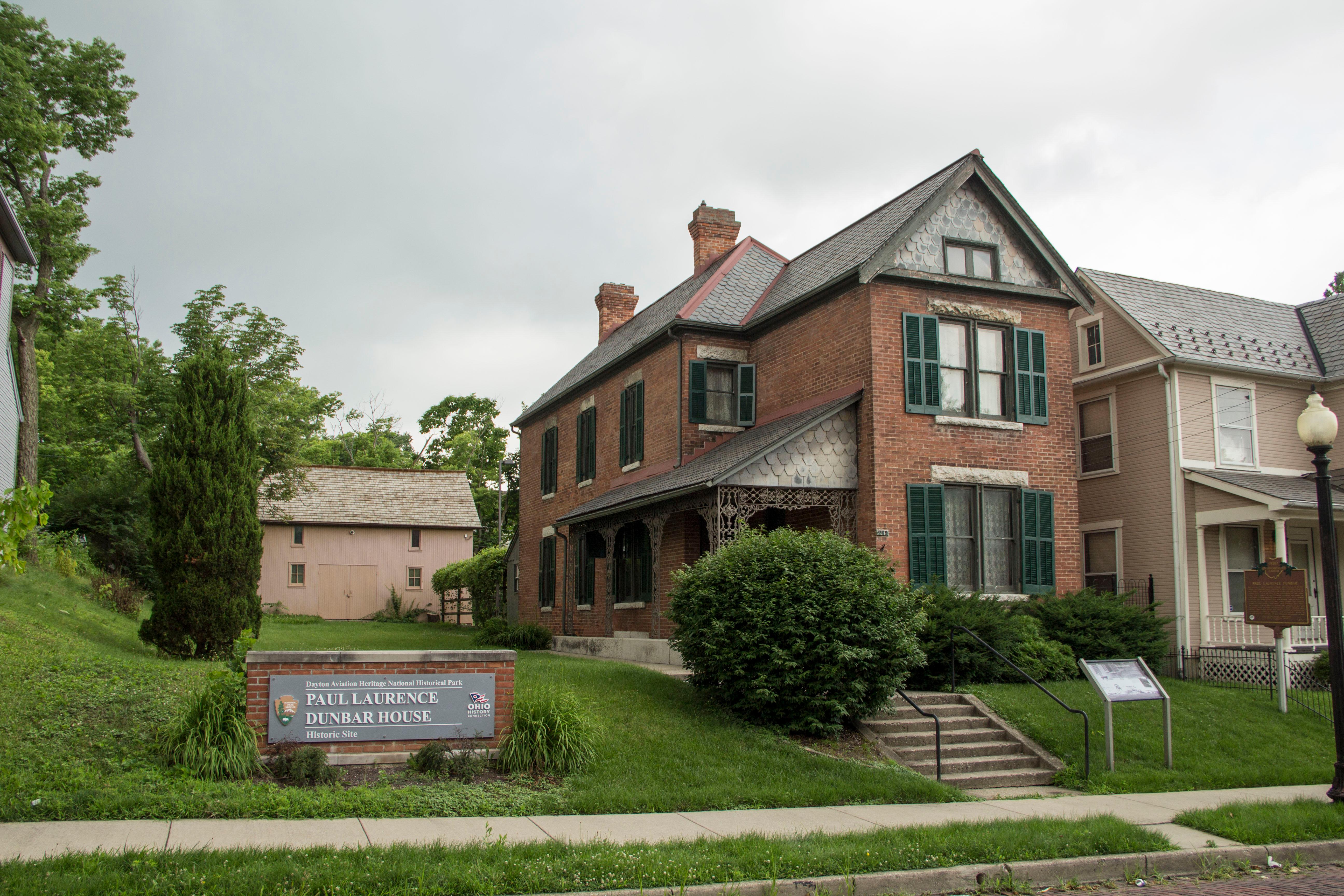 A two-story home with peaked gray roof and two chimneys with green shutters around the windows