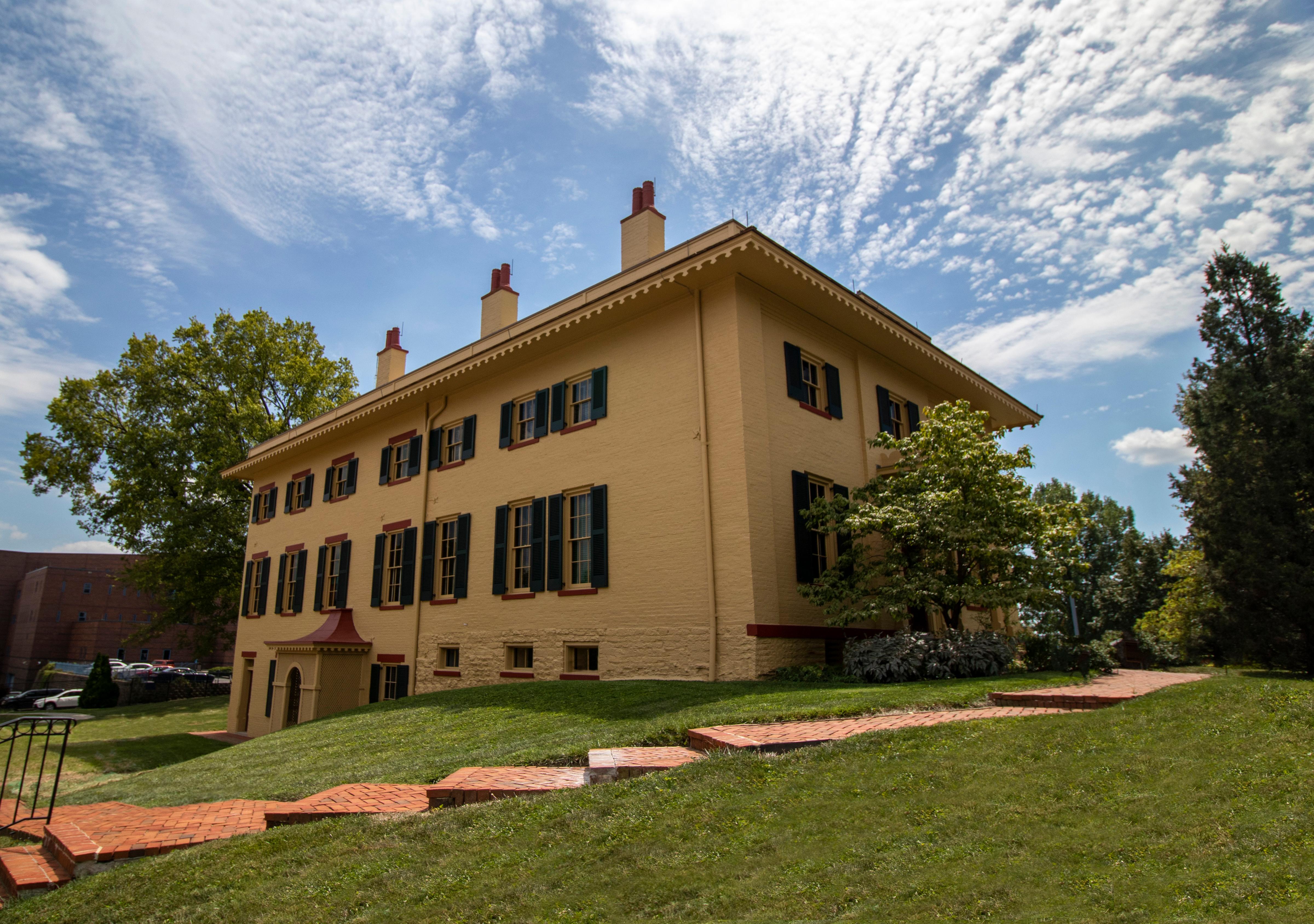 A yellow two-story brick building with tall windows and green shutters on them