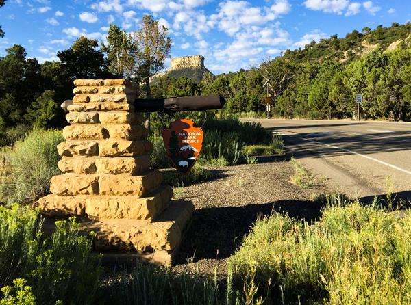 Sun strikes a wooden arrowhead-shaped sign along a road.