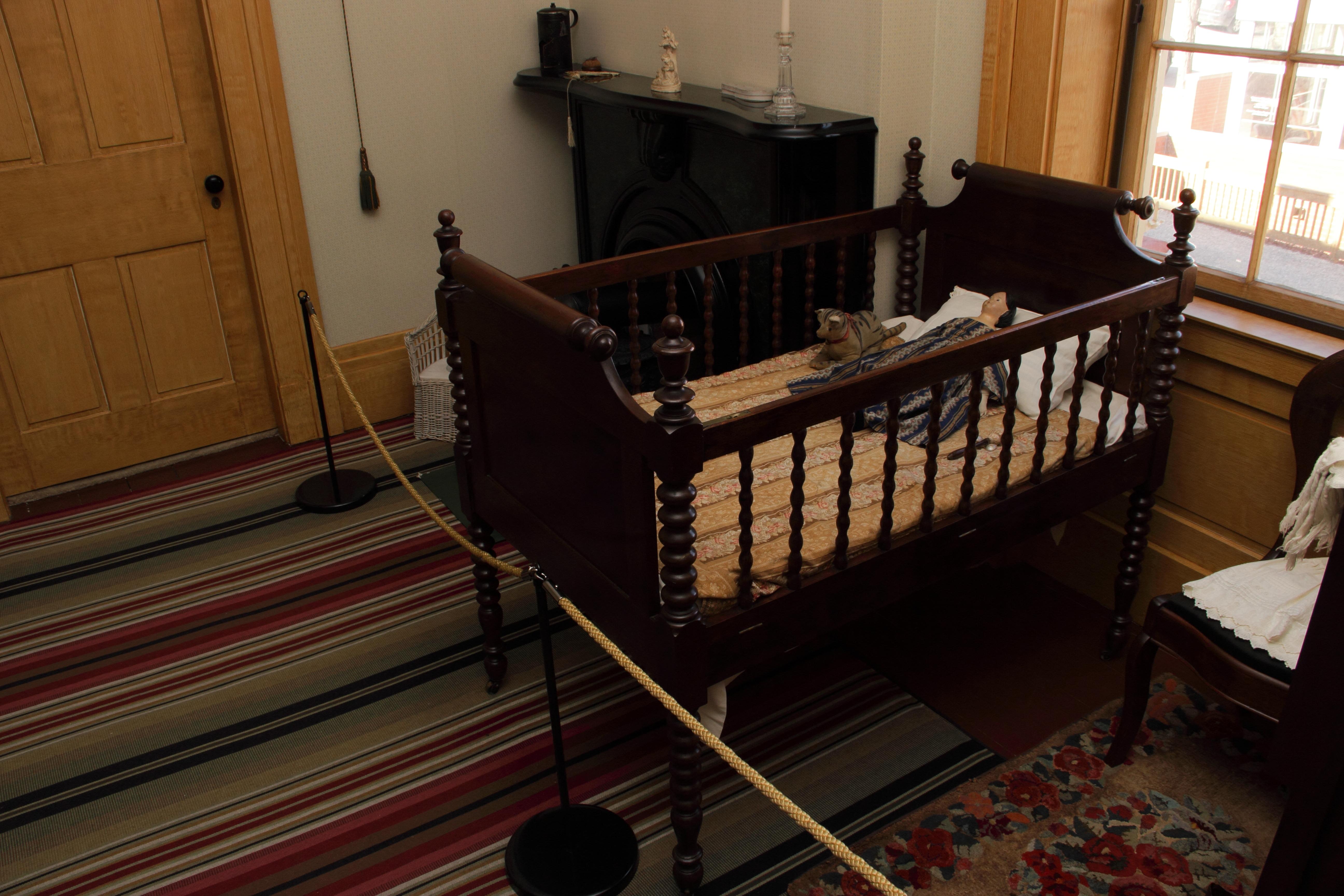 A dark wooden baby crib with wooden spindles sits inside of a bedroom.