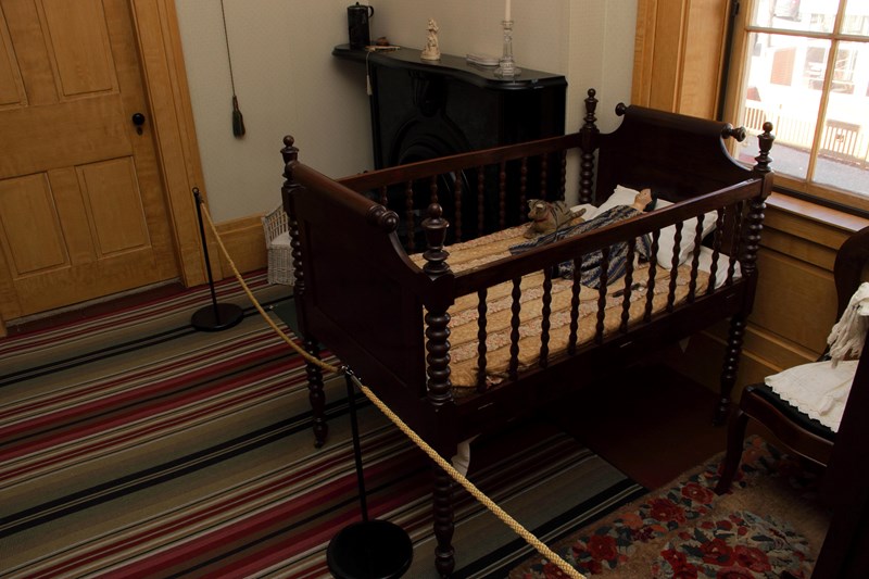 A dark wooden baby crib with wooden spindles sits inside of a bedroom.